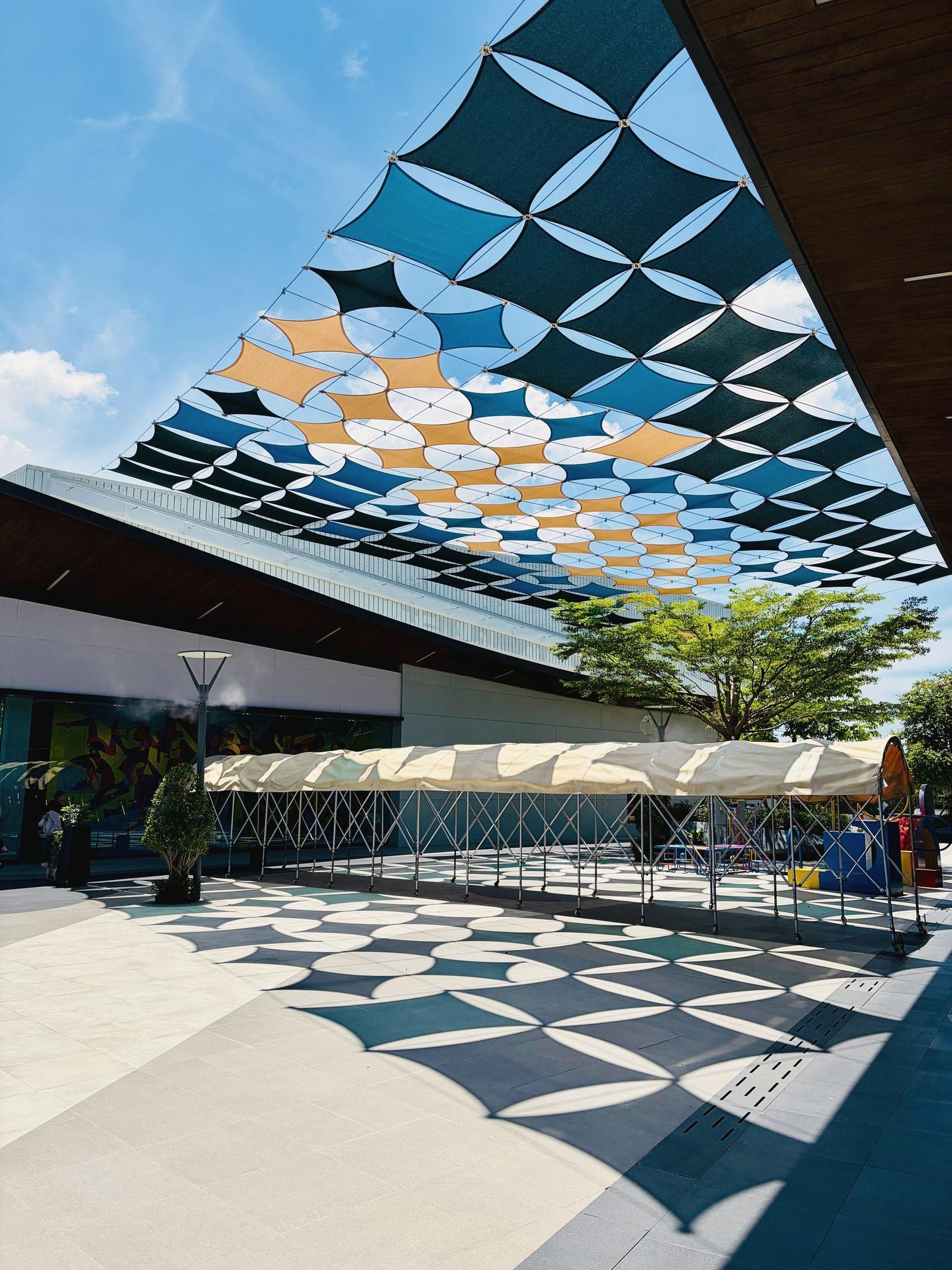 A geometric fabric shade canopy seen from below against the sky.